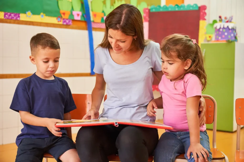 a childcare educator with two children reading a book