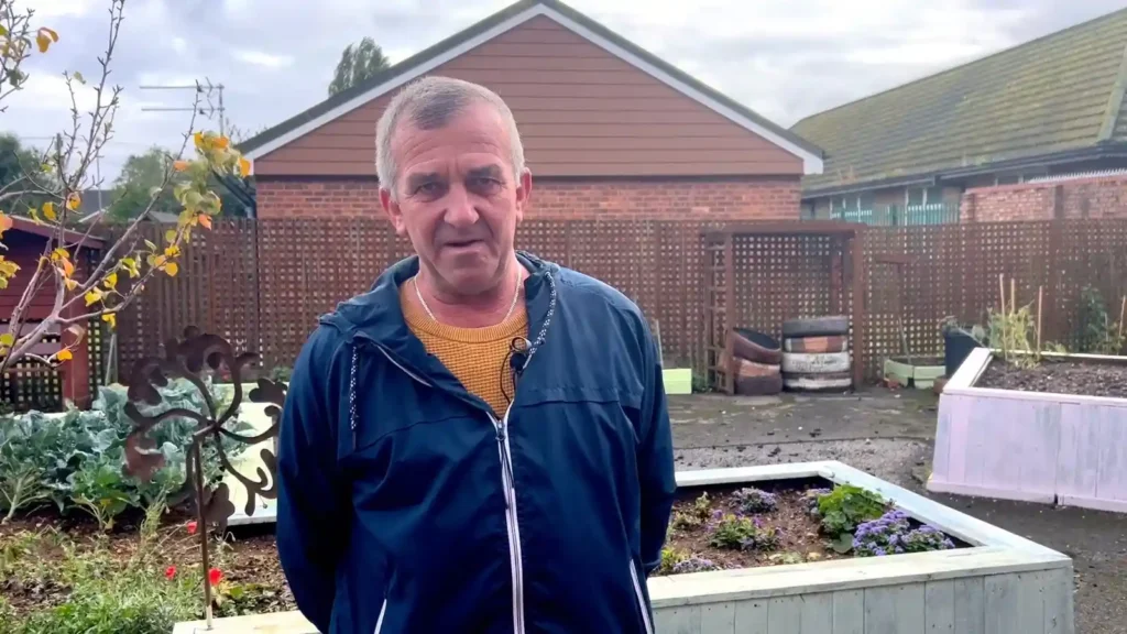 Anatoli is standing in his garden with his hands behind his back.