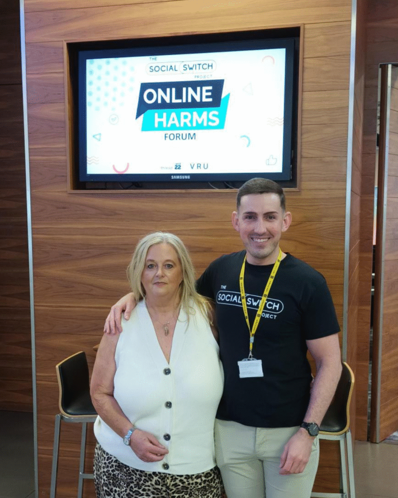 Jon Matthews and his apprenticeship tutor Andrea outside the Online Harms Forum venue with a Screen behind them showing the event details.